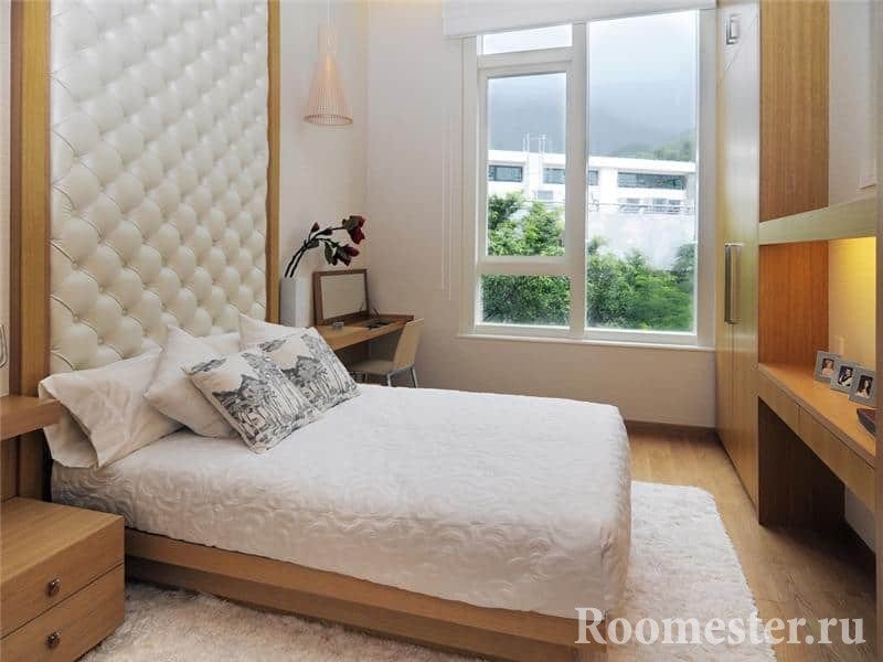Небольшая кровать с кожаным изголовьем и в спальне с большим окном